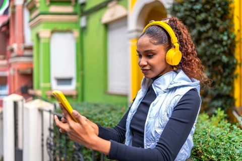 African american woman using phone while listening to music standing in a colorful street