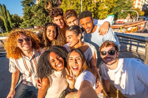 Multi-ethnic young casual and happy friends gesturing success while taking selfie in the city