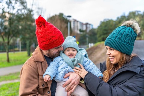 Parents holding their baby while smiling and enjoying a joyful winter day in a park, surrounded by