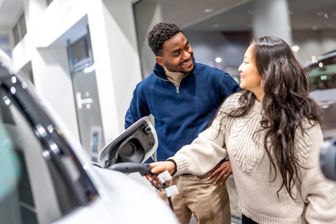 Smiling couple examining the charging socket of an electric vehicle while exploring options at a