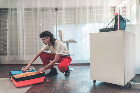 Young non-binary individual with a mullet haircut organizing beauty products in a trolley case,