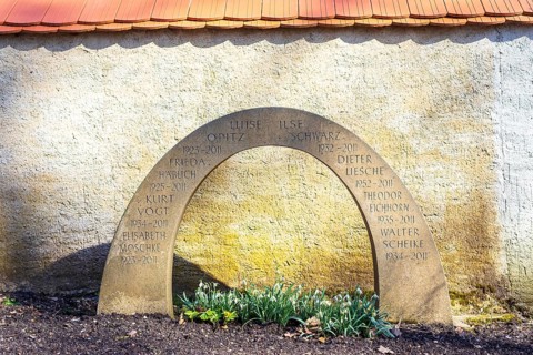 Gravestone in the shape of a rainbow on a communal urn grave, with snowdrops (galanthus) blooming