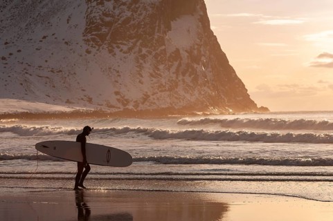 Surfer with surfboard under his arm on the beach of Unnstad, winter surfing, Lofoten Island