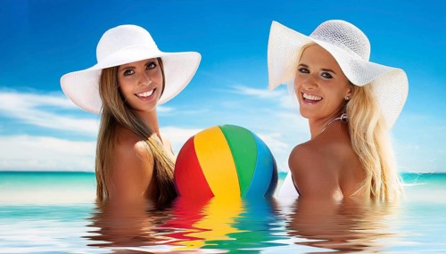 Two young woman in sun hats playing with a beach ball on the beach in the Caribbean