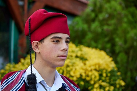 Side portrait of a boy in traditional Cretan traditional costume with a red hat outdoors, visit of