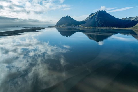 Aerial view over the calm sea to Mt. Brunnhorn and Vestrahorn, east of Höfn, clouds are reflected