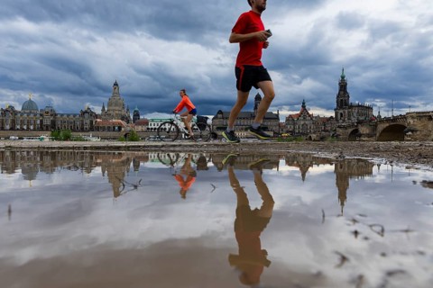 The silhouette of Dresden with a cyclist and a jogger and dark clouds behind the Church of Our