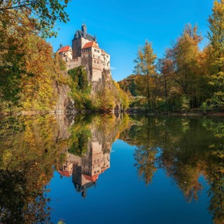 Kriebstein Castle near Mittweida surrounded by colourful forest in autumn, reflection in the river