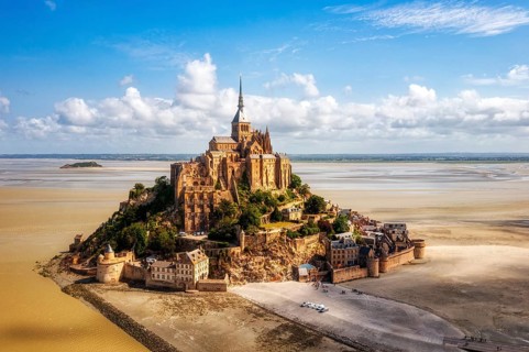 High-lying abbey on a rocky island, surrounded by sand and blue sky, Le Mont-Saint-Michel