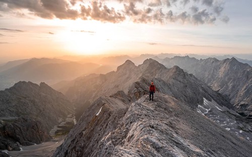 Mountaineer with helmet on a narrow rocky ridge at sunrise, crossing the Jubiläumsgrat, view of