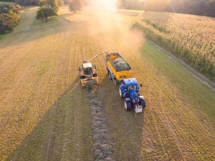Aerial view of a tractor and a harvester picking up hay in a field at sunset, Haselstaller Hof,