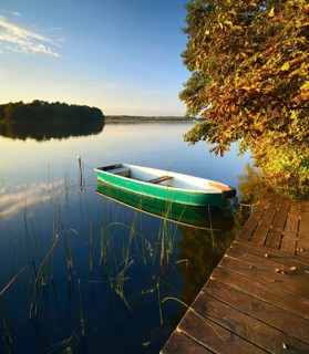 Quiet lake with jetty and rowing boat in the evening in autumn, horse chestnut with autumn leaves