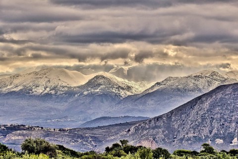 Snowy mountains under threatening grey clouds in a vast landscape with a dramatic atmosphere, Lefka