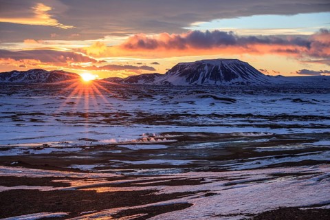 Hot springs and geothermal area in front of mountain landscape in winter, sunbeams, cloudy mood,