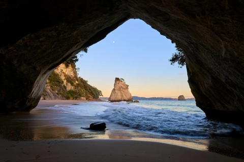 Cave opening shows a calm sea scene with rock formations in the twilight, Cathedral Cove,