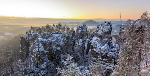 Snow-covered rock castle Neurathen and Bastei bridge in the morning, in the background the