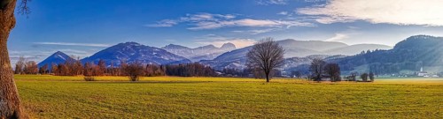 Wide green meadow in front of a mountain backdrop under a blue sky with light clouds, Bad Feilnbach