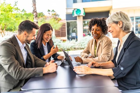 Side view of multi-ethnic happy business people in a meeting using laptop sitting in a cafeteria