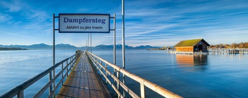 Steamer jetty and boathouse on Lake Chiemsee in autumn in the morning light, behind the Chiemgau