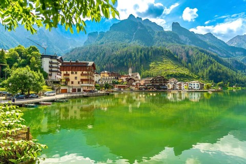 Tranquil summer scene of alleghe village reflecting on the emerald waters of lake alleghe, nestled