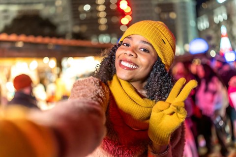 Smiling woman wearing winter clothes showing victory sign holding boyfriend's hand enjoying
