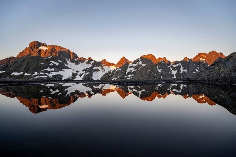 Rocky mountain peaks reflected in a small pond, mountain landscape with alpenglow at sunrise, at