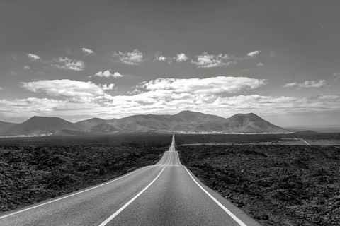 Empty endless country road through volcanic landscape, typical lava fields, Timanfaya National