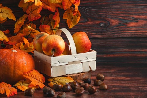 A wooden basket with apples next to chestnuts, a pumpkin and autumn leaves