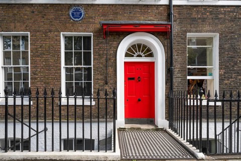 Red entrance door in a brick building with a cast-iron fence, Charles Dickens Museum, 48-49 Doughty