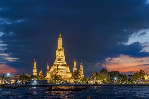 Wat Arun, Temple of Dawn at sunset with dark clouds. Boats on the Chao Phraya river. Tourist