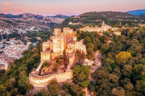 Aerial view of an Alhambra surrounded by trees at sunset in hilly terrain, Granada