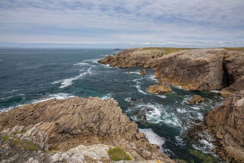 Rocky west coast of the Quiberon peninsula in Brittany, France, with a partly cloudy sky. Crashing