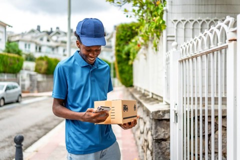 African delivery man using mobile while holding cardboard package to deliver
