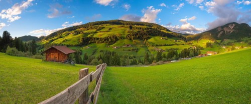 View along a wooden fence across a pasture to the mountains in the evening light, Dolomites, Odle