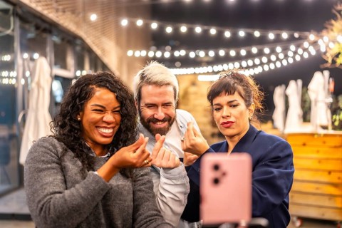 Multiracial diverse friends streaming online with a smartphone and gesturing love during night