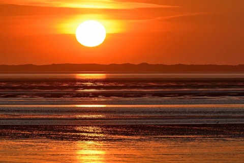 Sunset over the North Sea at low tide, the outline of the island of Juist on the horizon,