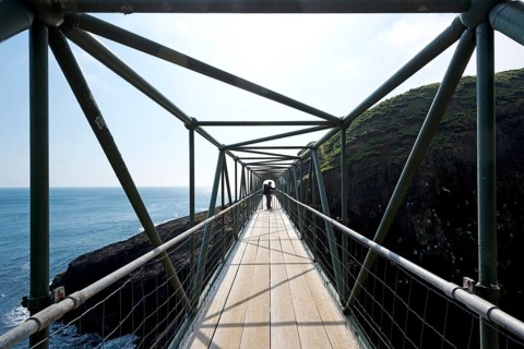Hiker standing on the so-called Atlantic Bridge, footbridge over a crevice Hólmgjógv, Mykines,