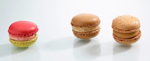 Three differently coloured macarons in front of a white background, studio shot