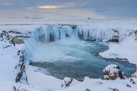 Icy waterfall and rapids in front of a mountain landscape, cloudy mood, snow, Godafoss, Iceland,