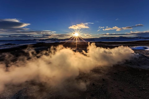 Hot springs and geothermal area in front of mountain landscape in winter, sunbeams, cloudy mood,