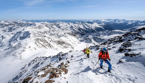 Ski tourer on foot, carrying skis on backpack, mountain panorama, snow-covered mountain landscape