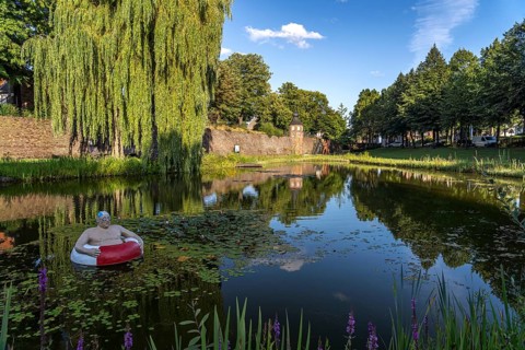 Frog pond with sculpture of Paul, the floating tyre man and the town wall with guard tower in Rees,