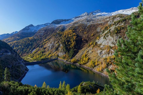 The Galgenbichl reservoir with a mountain forest in fall foliage on a bright sunny morning. Seen