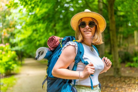 Cheerful caucasian young woman wearing sunglasses and sun hat carrying backpack walking along a