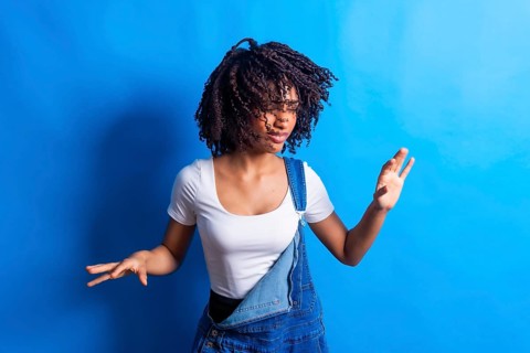 Young woman wearing casual clothes dancing with joy and moving her curly hair on a vibrant blue