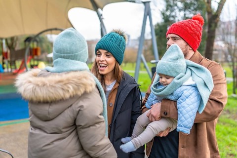 Parents and children enjoying playful moments together in winter attire at the playground, sharing
