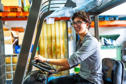 Side view of a happy caucasian woman with short hair and eyeglasses driving forklift in a
