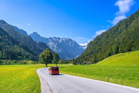 Red van driving along a winding road in the picturesque logarska dolina valley, surrounded by lush