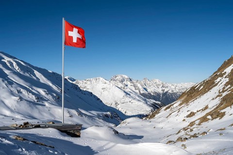 Swiss flag in front of mountain landscape in winter, mountain panorama with the peaks of the
