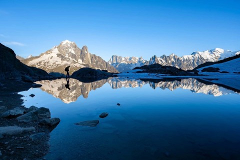 Mountaineer, silhouette in front of mountain landscape in the evening light, water reflection in
